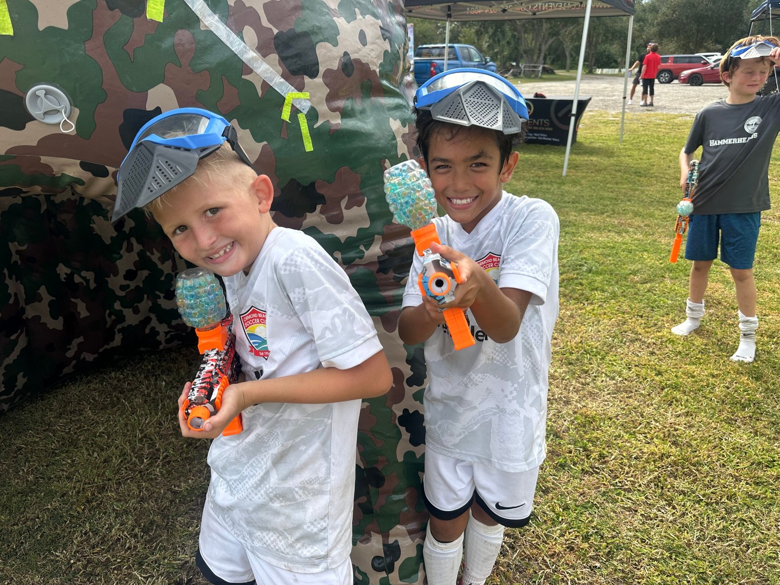 Smiling boys in soccer jerseys holding gel blasters next to a camo bunker at an All41Events gel blaster party in Orlando, FL